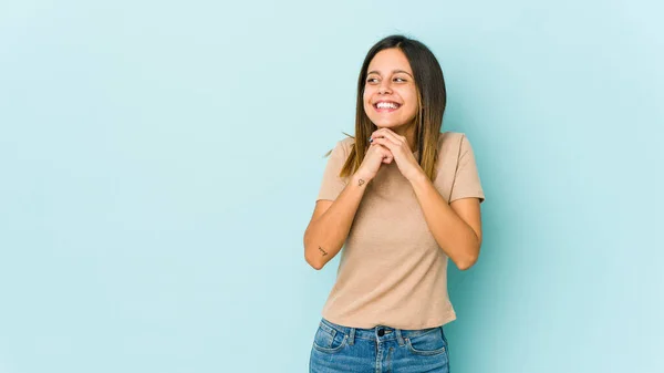 青の背景に隔離された若い女性は顎の下で手を維持し 喜んで脇を見ている — ストック写真