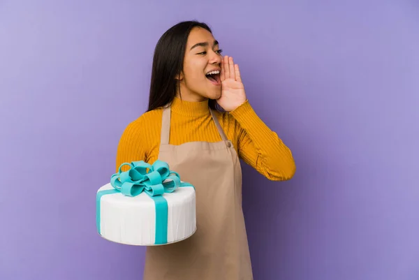 Young asian woman holding a cake isolated shouting and holding palm near opened mouth.