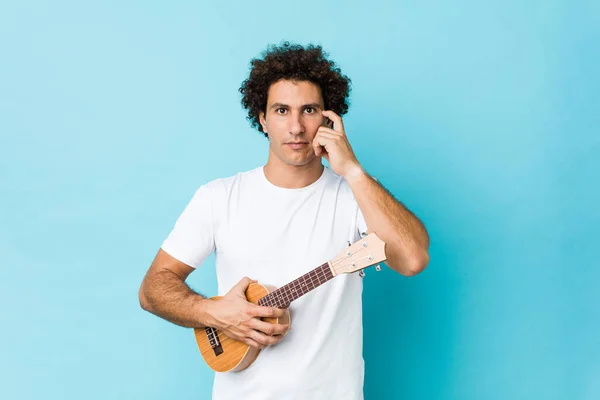 Young Caucasian Curly Man Playing Ukelele Pointing His Temple Finger — Stock Photo, Image