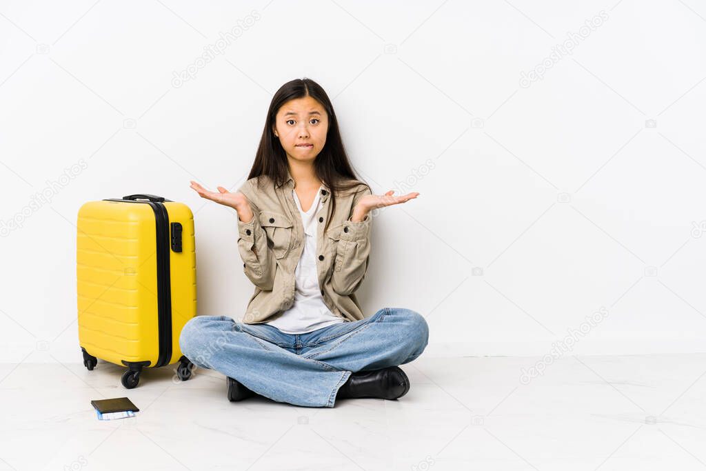 Young chinese traveler woman sitting holding a boarding passes confused and doubtful shrugging shoulders to hold a copy space.