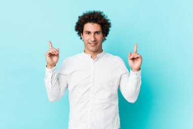 Zarif bir gömlek giyen genç, kıvırcık, olgun bir adam her iki elini de boş bir alan göstererek gösterir..