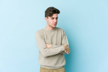 Kafkasyalı genç adam mavi arka planda izole edilmiş şüpheli, belirsiz, seni muayene ediyor..
