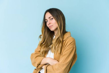 Kafkasyalı genç bir kadın mavi arka planda izole edilmiş şüpheli, belirsiz, seni muayene ediyor..