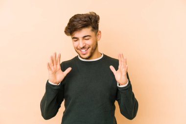 Genç Arap bir adam bej bir arka planda izole edilmiş neşeli bir şekilde gülüyor. Mutluluk kavramı.