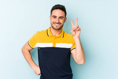 Mavi arka planda izole edilmiş genç beyaz adam iki numarayı parmaklarıyla gösteriyor..