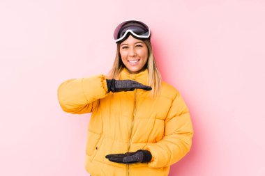 Pembe arka planda kayak kıyafeti giyen beyaz bir kadın iki eliyle bir şey tutuyor, ürün sunumu..