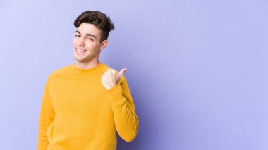 Mor arka plan noktalarında izole genç beyaz adam başparmak uzakta, gülüyor ve kaygısız.