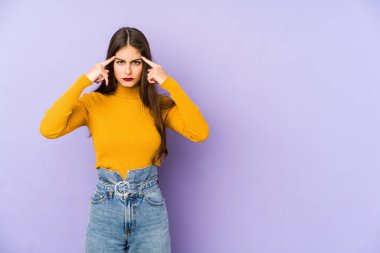 Mor arka planda izole edilmiş genç beyaz kadın bir göreve odaklanmış, parmaklarını işaret ediyor..