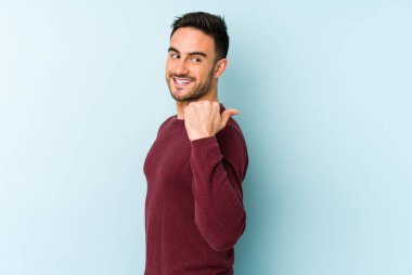 Kafkasyalı genç adam mavi arka plan noktalarında izole edilmiş başparmak uzakta, gülüyor ve kaygısız.