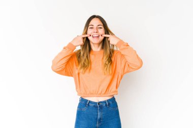 Beyaz arka planda izole edilmiş genç beyaz kadın gülümsüyor, parmaklarını ağıza doğrultuyor..