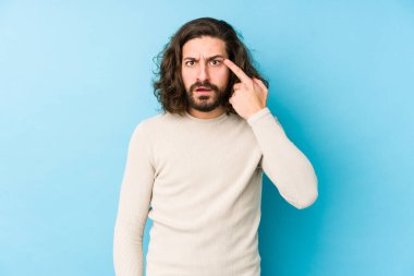 Mavi arka planda izole edilmiş genç, uzun saçlı adam işaret parmağıyla hayal kırıklığı jesti gösteriyor..