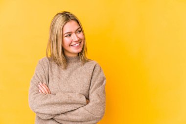 Sarışın, beyaz bir kadın, sarı arka planda izole edilmiş, kollarını kavuşturarak gülümsüyor..