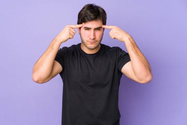 Mor arka planda izole edilmiş genç bir adam bir göreve odaklanmış, işaret parmaklarını başını işaret ediyor..