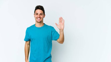 Beyaz arka planda izole edilmiş genç beyaz bir adam gülümseyerek beş numarayı parmaklarıyla gösteriyor..