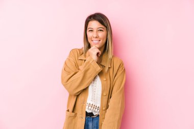 Kafkasyalı genç bir kadın yalnız poz veriyor gülümsüyor ve kendine güveniyor, elleriyle çenesine dokunuyor..