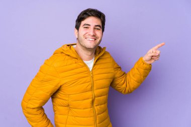 Mor arka planda izole edilmiş genç adam işaret parmağıyla işaret ederek gülümsüyor..