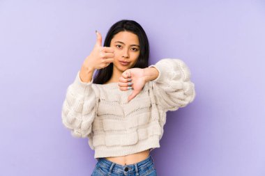 Mor arka planda izole edilmiş genç Çinli bir kadın baş parmağını kaldırıyor ve baş parmağını aşağı gösteriyor, zor seçim konsepti.
