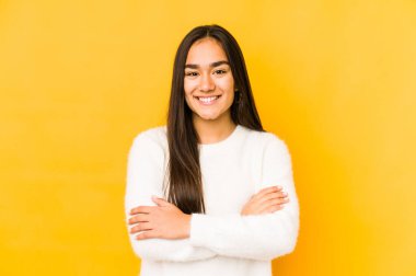 Sarı arka planda izole edilmiş genç bir kadın kendinden emin, kararlılıkla kollarını kavuşturuyor..