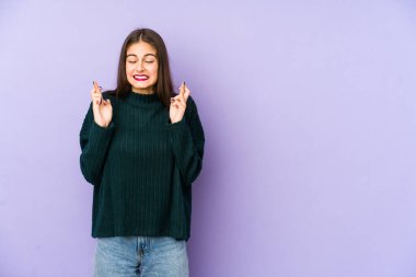 Mor arka planda izole edilmiş beyaz bir kadın şans dilemek için parmaklarını çapraz yapıyor.
