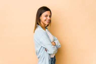 Bej arka planda izole edilmiş, kendinden emin, kararlılıkla kol kola geçen genç bir kadın..