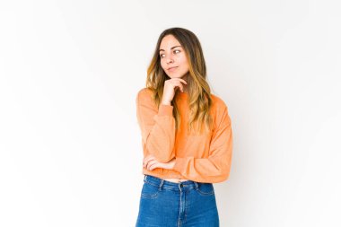 Beyaz arka planda soyutlanmış beyaz tenli genç bir kadın şüpheli ve şüpheci bir ifadeyle yana bakıyor..