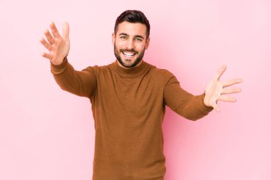 Pembe arka planı olan genç beyaz bir adam kameraya sarıldığı için kendini güvende hissediyor..