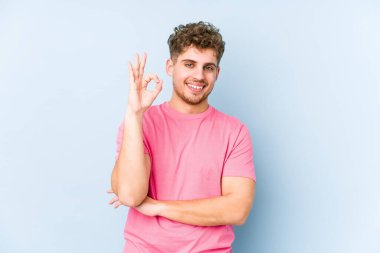 Sarışın, kıvırcık saçlı, beyaz tenli bir adam göz kırpıyor ve elinde iyi bir jest tutuyor..