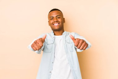 Genç latin adam bej arka planda izole edildi. Başparmaklar yukarı, bir şey için tezahürat, destek ve saygı konsepti..