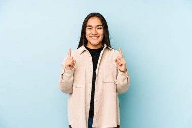 Mavi arka planda izole edilmiş genç bir kadın iki parmağı da boş bir alan gösteriyor..