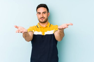 Mavi arka planda izole genç beyaz adam kollarıyla ölçek yapar, mutlu ve kendinden emin hisseder..