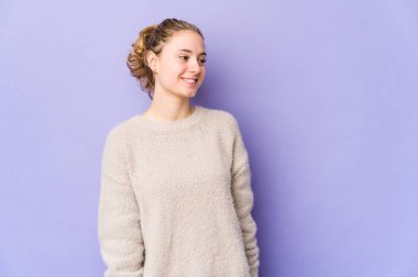 Mor arka planda genç beyaz bir kadın gevşemiş ve mutlu bir şekilde gülüyor, boynunda dişlerini gösteriyor..