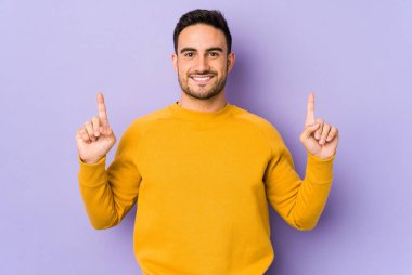 Mor arka planda izole genç beyaz adam iki ön parmağı da boş bir alan gösteriyor..