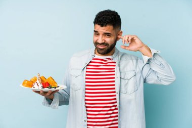 Genç latin adam waffle tutuyor, kulaklarını elleriyle kapatıyor..