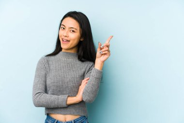 Mavi bir arka planda izole edilmiş genç Çinli kadın işaret parmağıyla işaret ederek gülümsüyor..