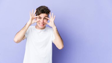 Mor arka planda izole edilmiş genç beyaz adam bir başarı fırsatı bulmak için gözlerini açık tutuyor..