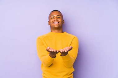 Mor arka planda izole edilmiş genç bir latin adam elinde avuç içi bir şeyle kameraya sunuyor..