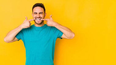 Sarı fırında izole edilmiş genç beyaz adam gülümsüyor, parmaklarını ağıza doğrultuyor..