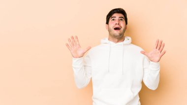 Bej arka planda izole edilmiş genç adam gökyüzüne haykırıyor, yukarı bakıyor, hayal kırıklığına uğramış..