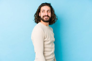 Uzun saçlı, mavi bir arka planda izole bir genç. Gülümsüyor, neşeli ve keyifli görünüyor..