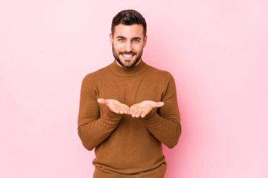 Pembe arka planda genç beyaz bir adam avuçlarıyla bir şey tutarak kameraya sunuyor..