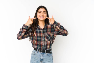 Mor arka planda izole edilmiş genç Hintli kadın gülümsüyor, parmaklarını ağzına doğrultuyor..