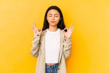 Sarı arka planda izole edilmiş genç Çinli kadın sıkı çalışma gününden sonra rahatlıyor, yoga yapıyor..