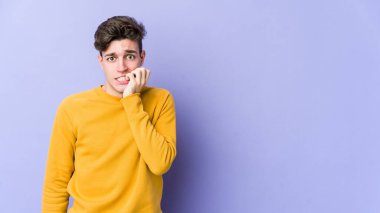 Mor arka planda izole edilmiş, tırnak yiyen, gergin ve endişeli genç bir beyaz adam..