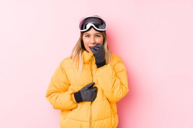 Pembe arka planda kayak kıyafeti giyen, tırnaklarını yiyen, gergin ve endişeli beyaz bir kadın..