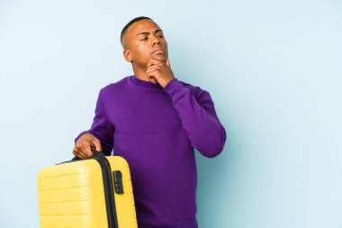 Elinde bavul tutan genç bir gezgin şüpheli ve şüpheci bir ifadeyle yana bakıyor..