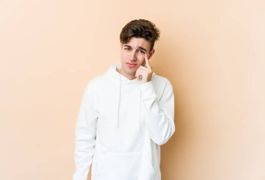 Beyaz tenli genç adam bej arka planda izole edilmiş ağlıyordu, bir şeyden mutsuzdu, ıstırap ve kafa karışıklığı vardı..