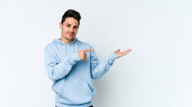 Beyaz arka planda izole edilmiş genç beyaz bir adam, palmiye üzerinde bir fotokopi alanı tutarken heyecanlı..