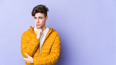 Mor arka planda izole edilmiş genç beyaz adam alaycı bir ifadeyle kameraya bakarken mutsuz oluyor..