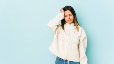 Mavi arka planda izole edilmiş genç bir kadın yorgun ve uykulu. Elini başının üstünde tutuyor..