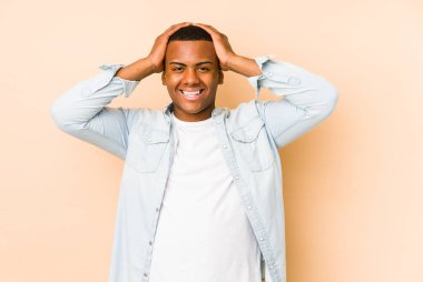 Bej arka planda izole edilmiş genç latin adam, mutlu bir şekilde ellerini başının üstünde tutuyor. Mutluluk kavramı.